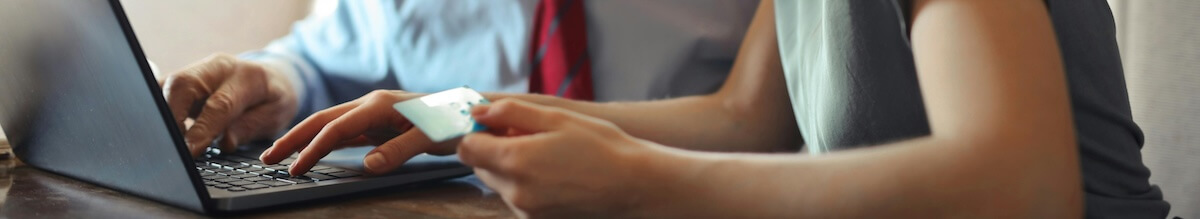 Two people work on a a laptop together. One of them holds a credit card