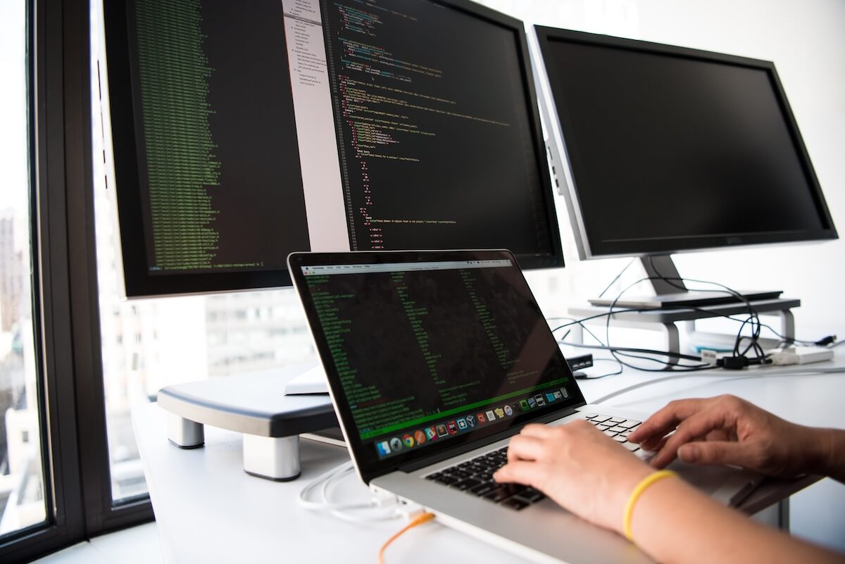 Developer writing code on a laptop, their laptop is plugged into multiple monitors.